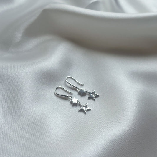 A pair of sterling silver dangle earrings with a star design, placed on a white silky surface.