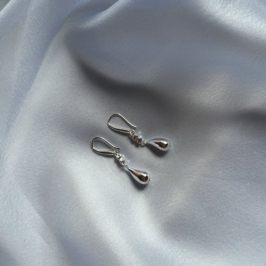 A pair of handmade sterling silver teardrop-shaped earrings laid on a silky surface.